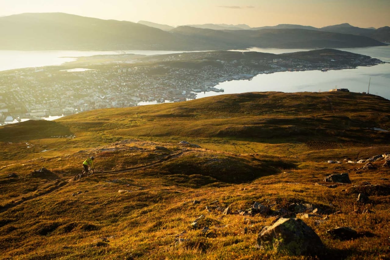 Stien går fra toppen Bønntua ned til Fjellheisen (til høyre i bildet) for så å traversere tilbake og ned til Tromsø. / Stisykling i Norge.