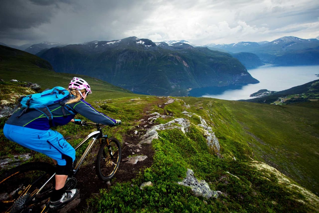 Ned fra Mefjellet byttes etterhvert fjordutsikt ut mot tett skog. Like bratt er det dog. / Stisykling i Norge.